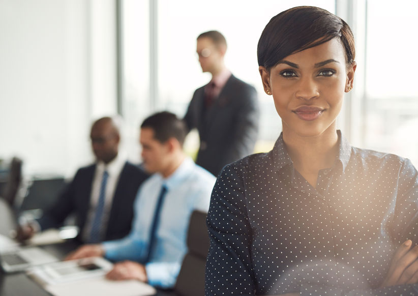 What Does Success Look Like to You? 9 Young grinning business owner in office with polka dot blouse, folded arms and confident expression in front of group of mentees at conference table