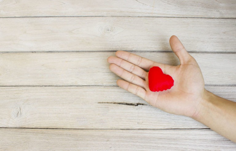 Virtual Mentoring in the Age of Social Distancing 6 A human hand holding a small red stuffed shaped heart in their palm against a wood plank background.