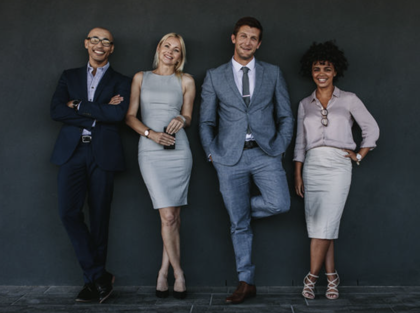 Mentoring Outside the Box 4 Four business people smiling and leaning up against a wall