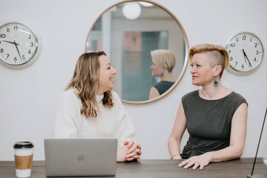 What Is Micro-Mentoring? Definition, Benefits, and Examples 3 Two women sitting at a table in deep discussion during a micro-mentoring session in an office.