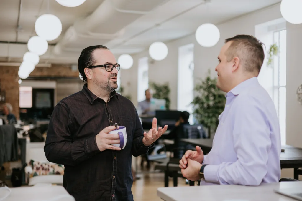 5 Types of Mentoring Program Formats (with Detailed Use Cases) 7 Two men in an office talking about mentoring.