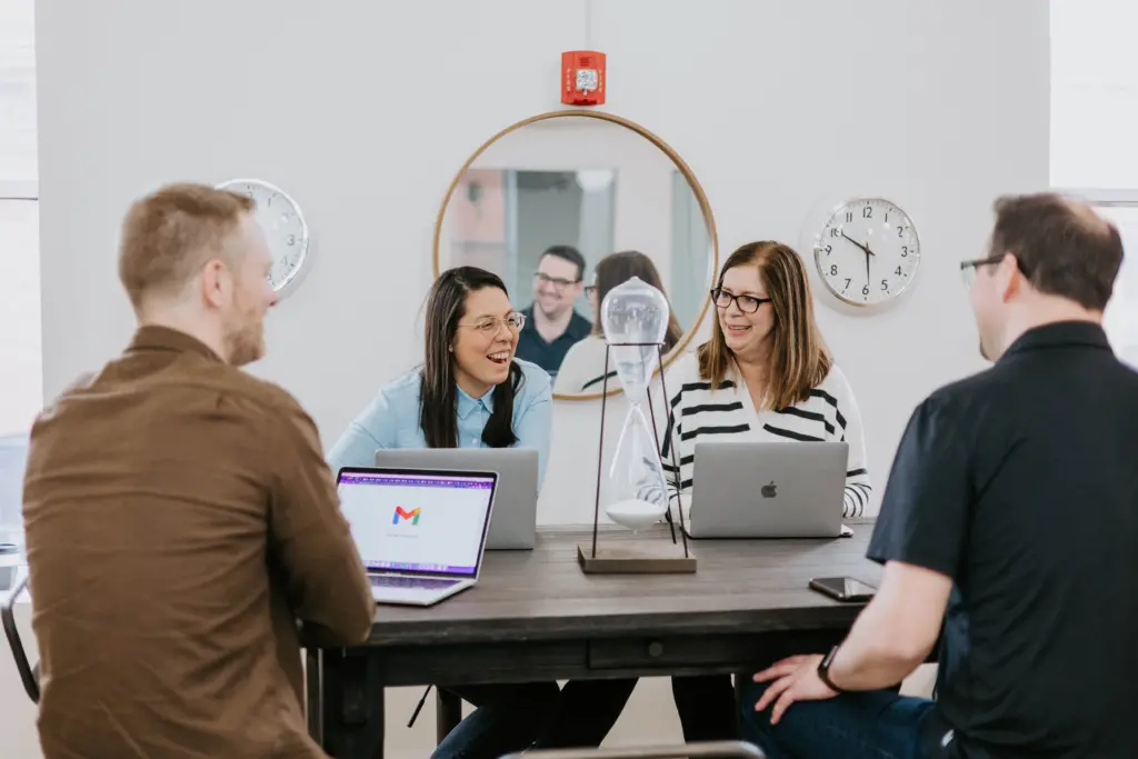What Is Employee Development? In-Depth Strategy Guide 4 Workers sitting at a table engaged in collaborative employee development with laptops open.