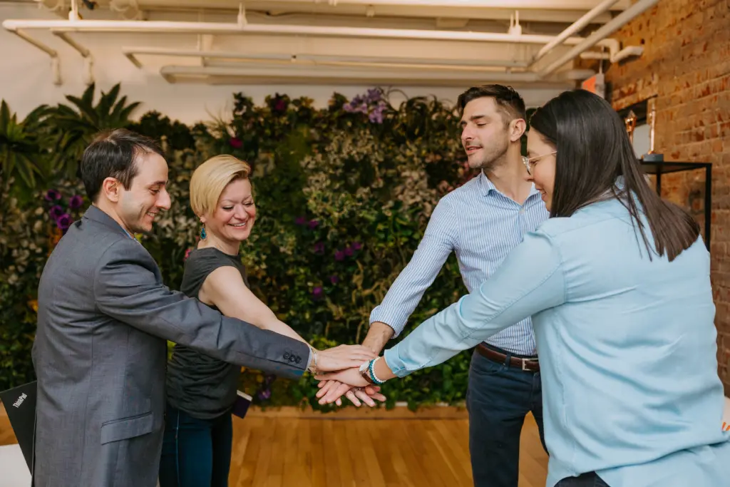 Steward Leadership: Redefining Leadership for the Future Workplace 6 Group of employees in an office doing a team high huddle with hands together.