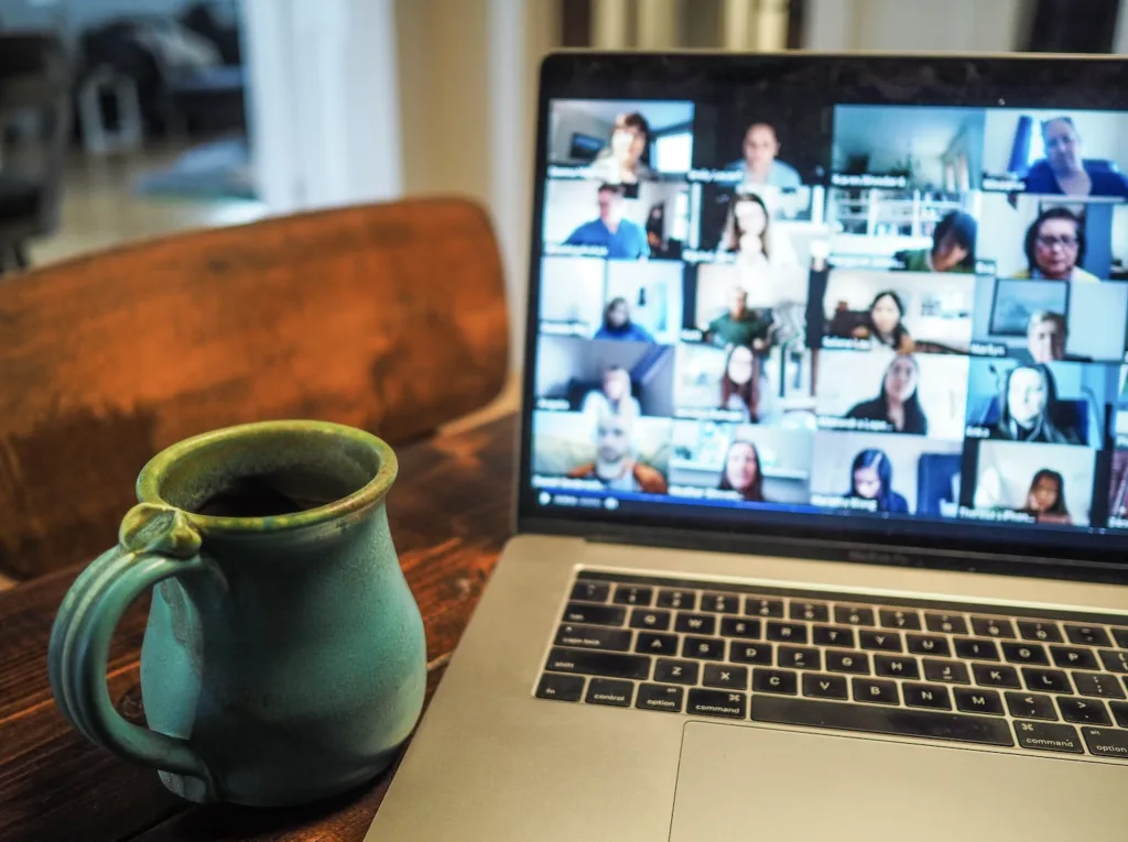 Virtual Mentoring in the Age of Social Distancing 5 Home office setting. Turquoise clay coffee mug sitting beside an open laptop. Laptop is displaying a virtual mentoring meeting with other mentors and mentees.