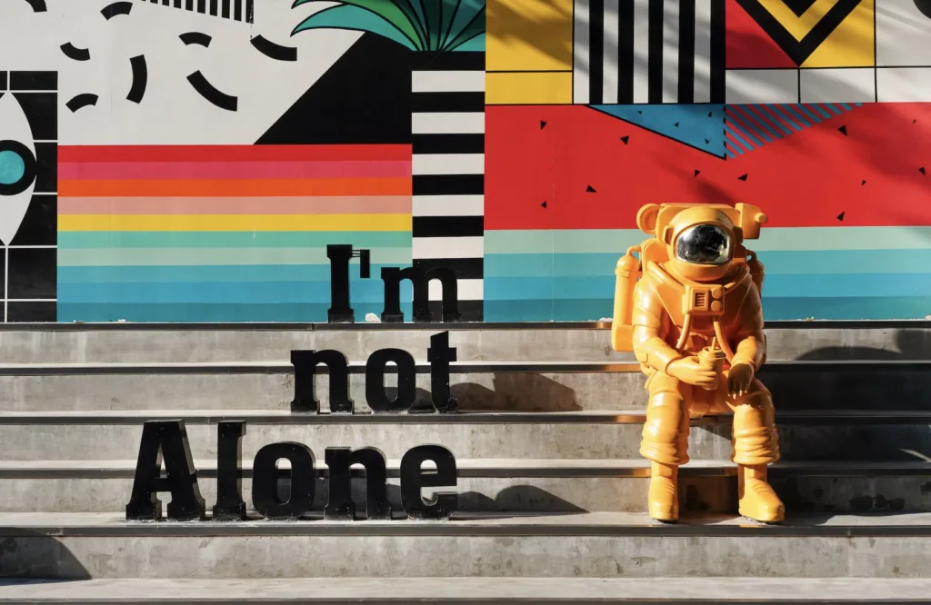 My Mentoring Mantra 4 Artistic image of an orange astronaut sitting on concrete steps sitting by a sign that says "I'm Not Alone"