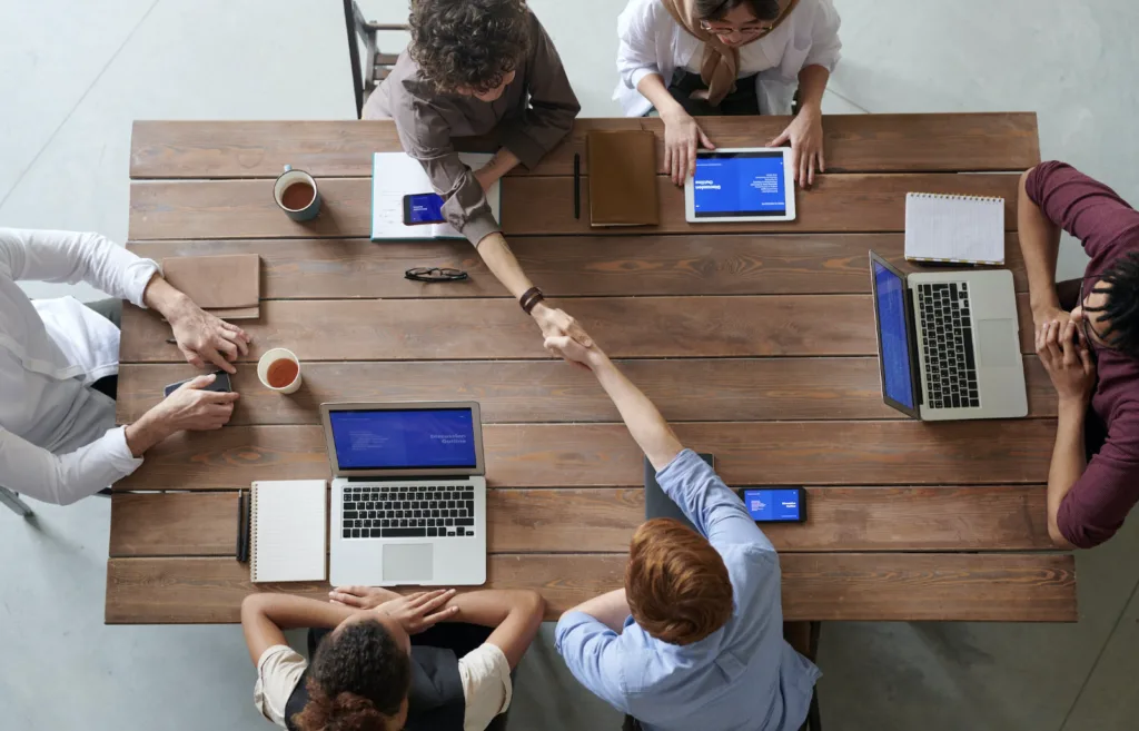 10 Essential Steps to Promote a Knowledge Sharing Culture 7 Workers at a table shaking hands after knowledge sharing.
